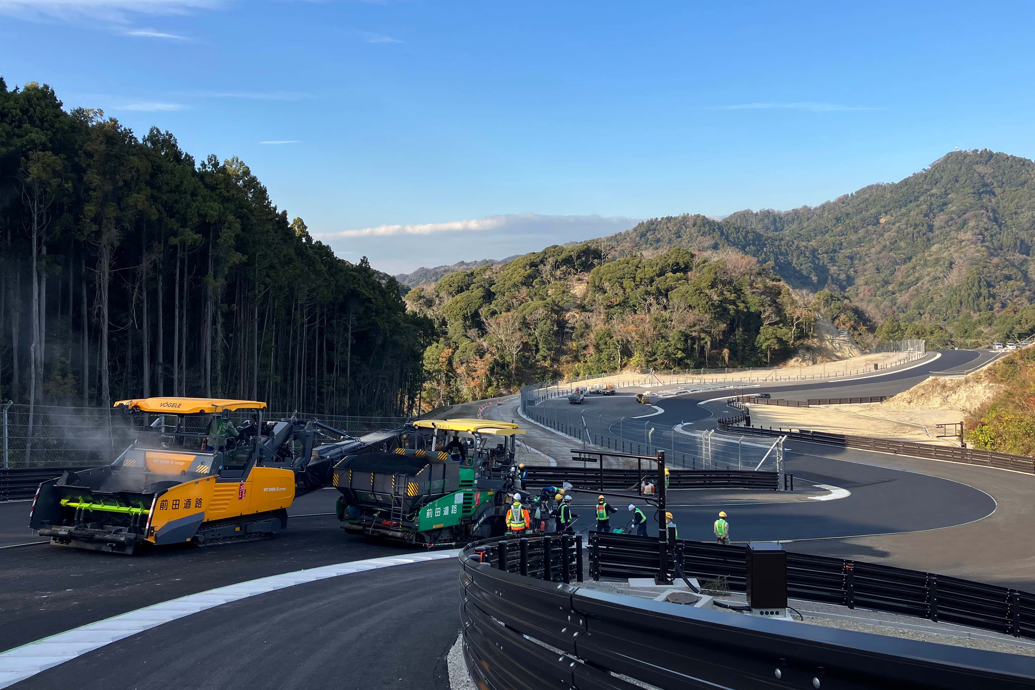 Pavement Maintenance & Repair Heavy asphalt paving machinery laying fresh blacktop on a winding curved road along a forested mountain slope